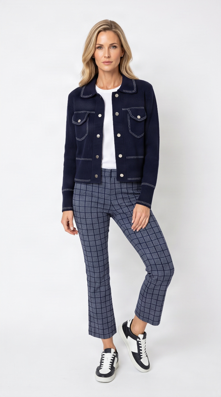 A woman modeling a dark navy cropped denim jacket with contrast stitching, paired with navy and gray plaid cropped trousers, a white t-shirt, and black and white sneakers, against a light gray studio background.