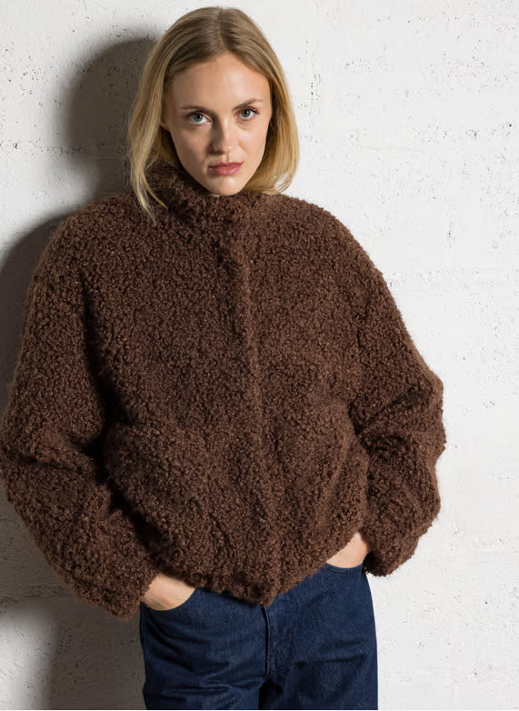 Person wearing a brown textured sweater against a white wall